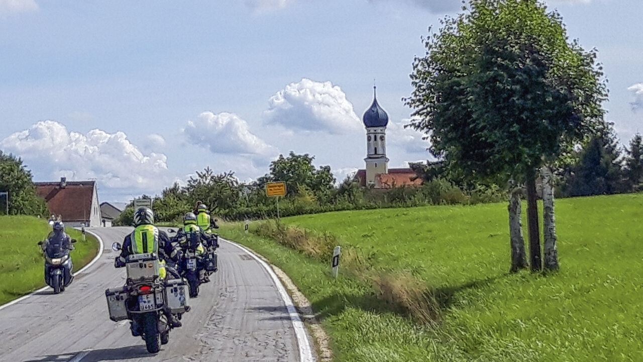 Motorradgruppe auf einer Landstraße, am Rand eine Kirche mit Zwiebelturm Motorradgruppe auf einer Landstraße, am Rand eine Kirche mit Zwiebelturm